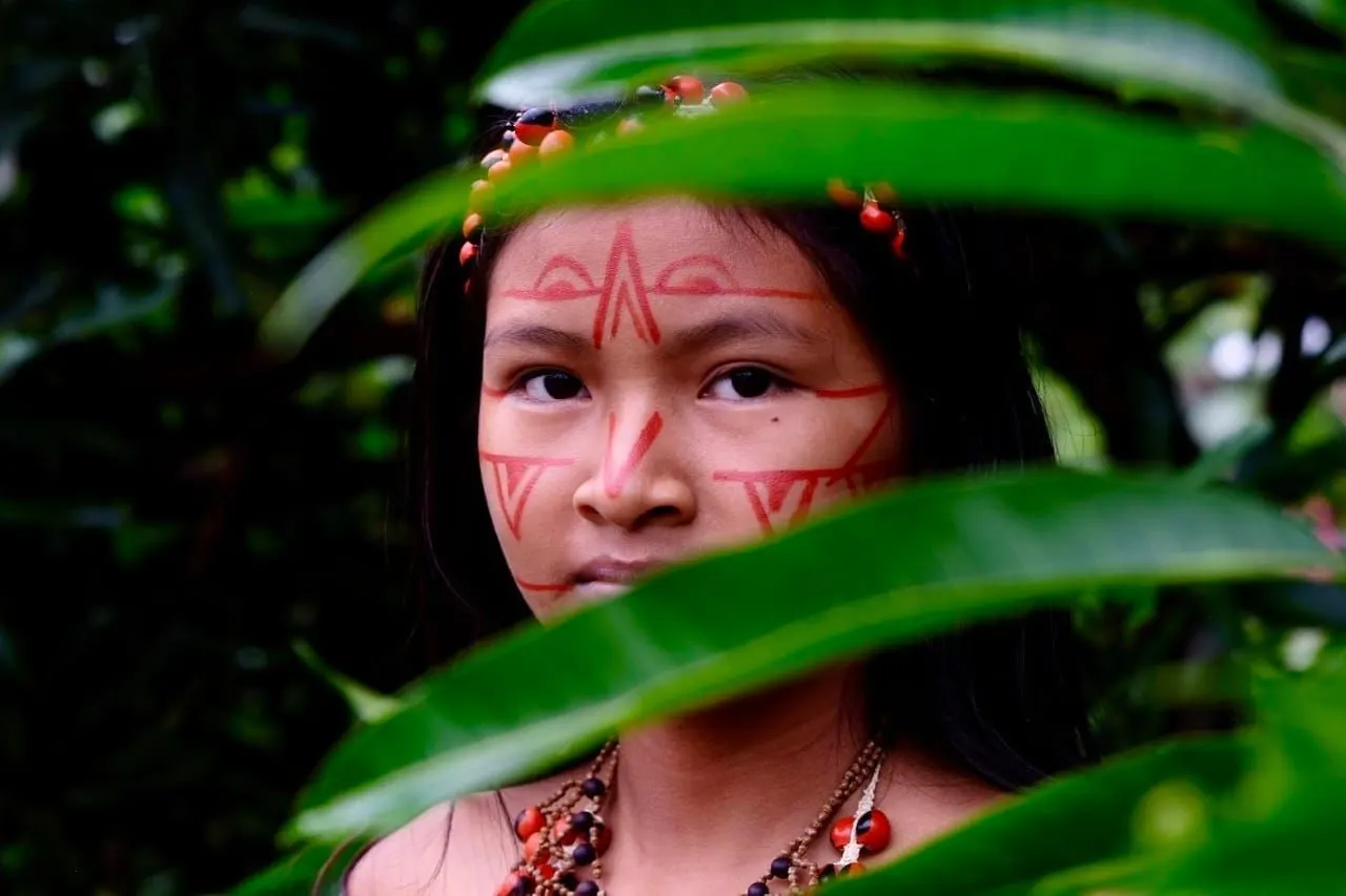 Niña kichwa con el rostro pintado con achiote, entre el follaje de la selva del Yasuní